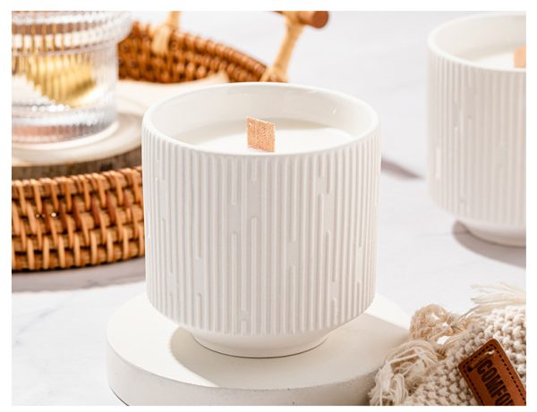 White ceramic soy candle with a wooden wick, placed on a minimalist white surface.