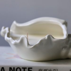 Seashell-shaped ceramic candle holder with wicks, placed on a book