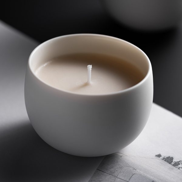 Minimalist white ceramic scented candle placed on an open book with a dark background.