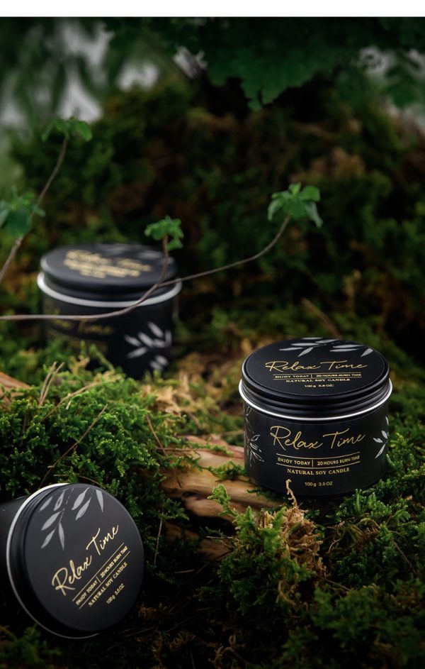 Relax Time Natural Soy Candle in a black tin container with botanical design, placed on a mossy forest floor.